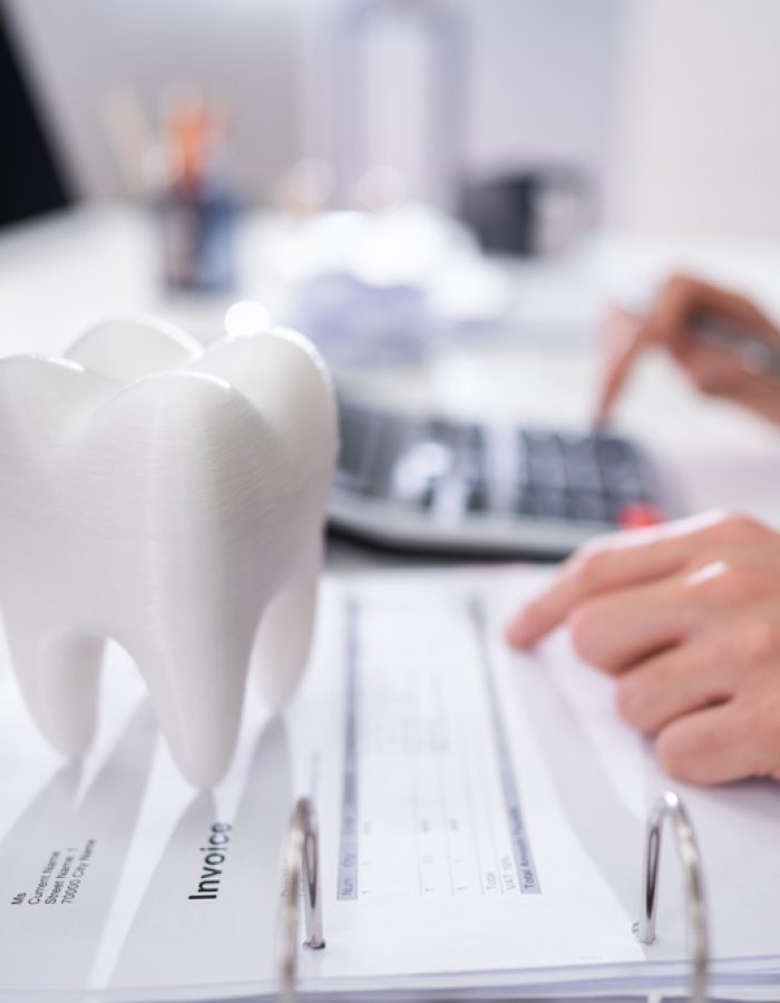 White Tooth In Front Of Man Calculating Bill Close-up Of Tooth In Front Of Businessperson Calculating Bill
